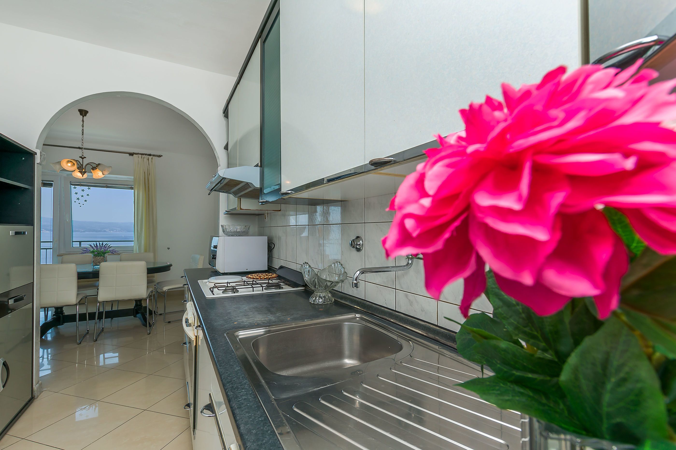 A modern kitchen with a stainless steel sink, white cabinets, and a dining area with a table and chairs.