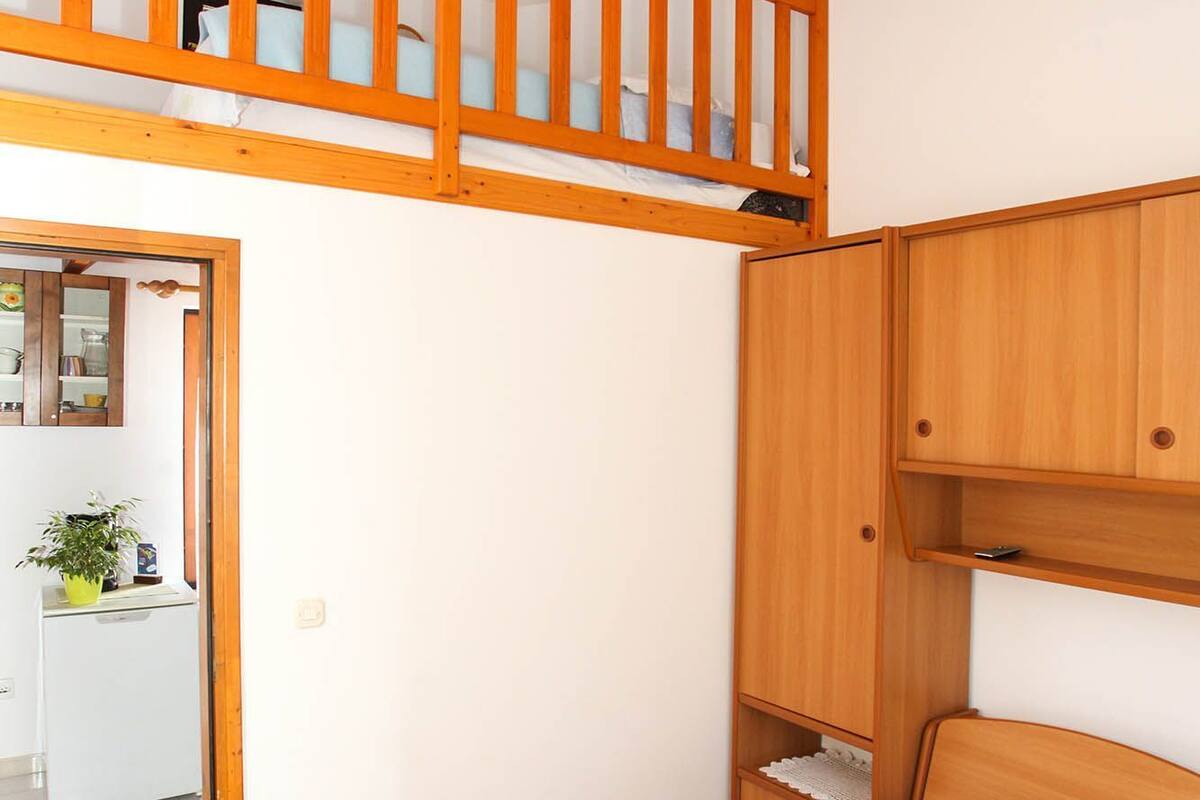Une chambre avec un lit superposé, une armoire en bois, une table de chevet et un petit coin cuisine.