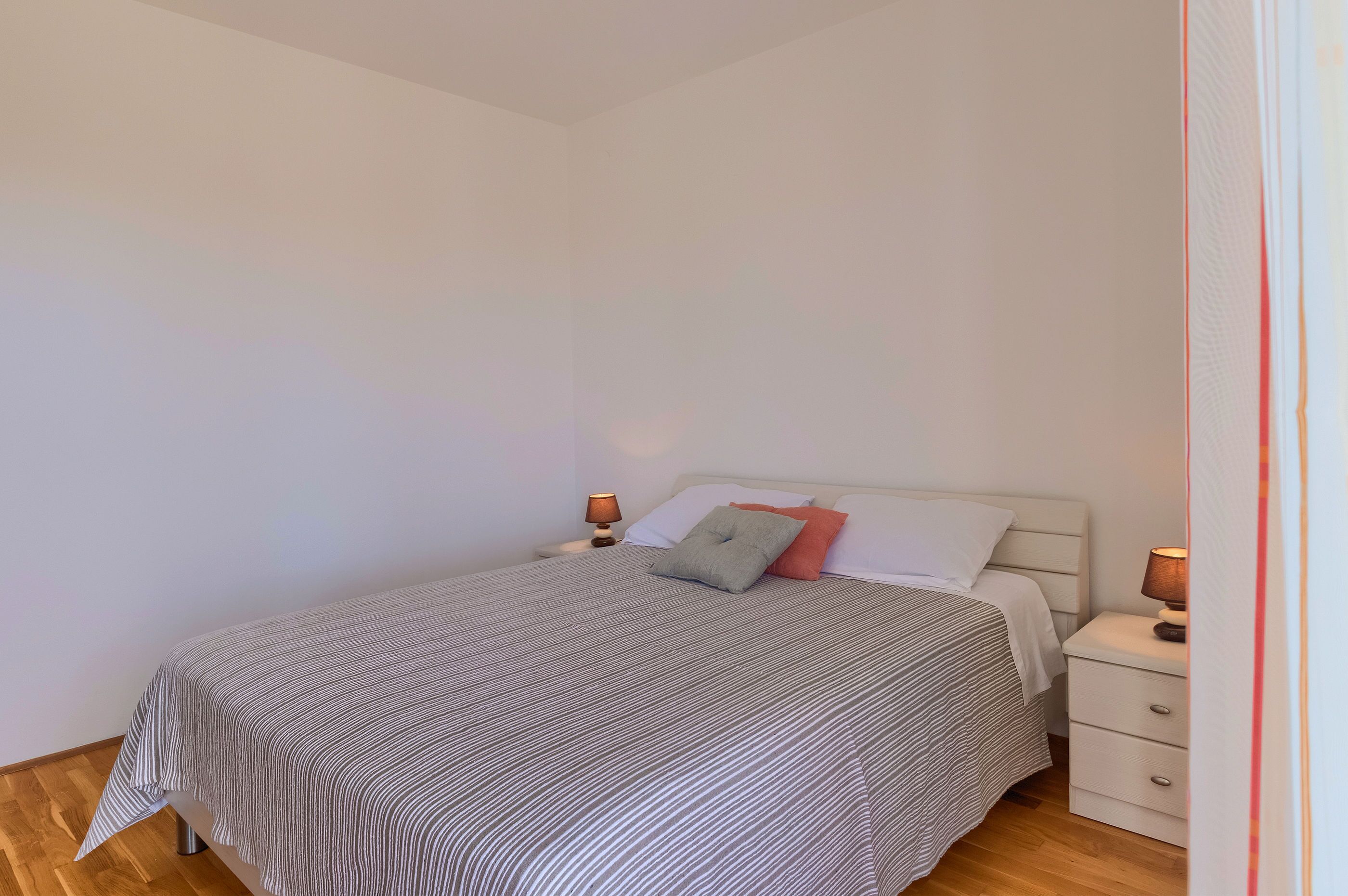 Una cama bien hecha con ropa de cama a rayas, dos mesitas de noche con lámparas y una mesita blanca.