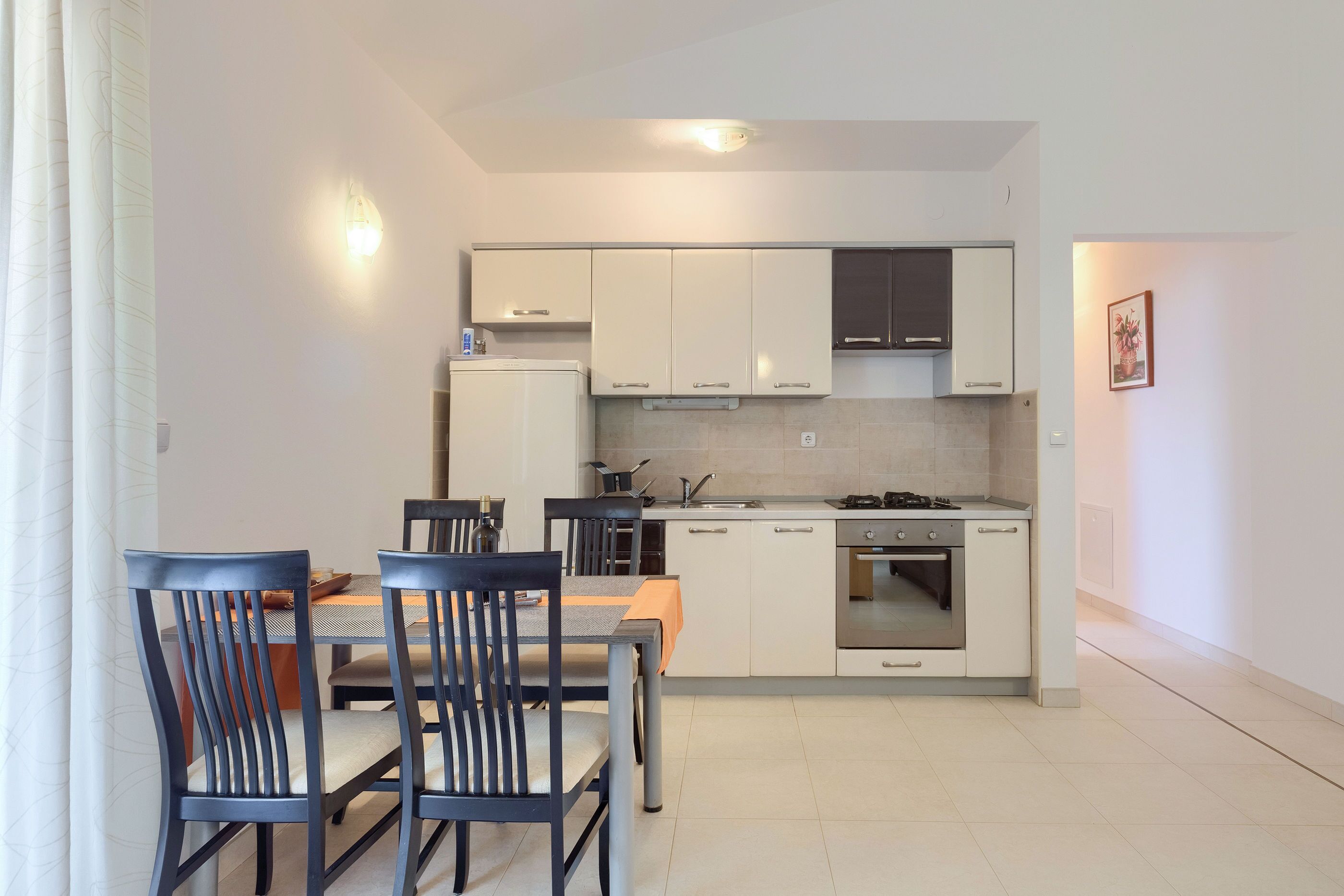 A modern kitchen with white cabinets, a dining table with chairs, and a built-in oven.