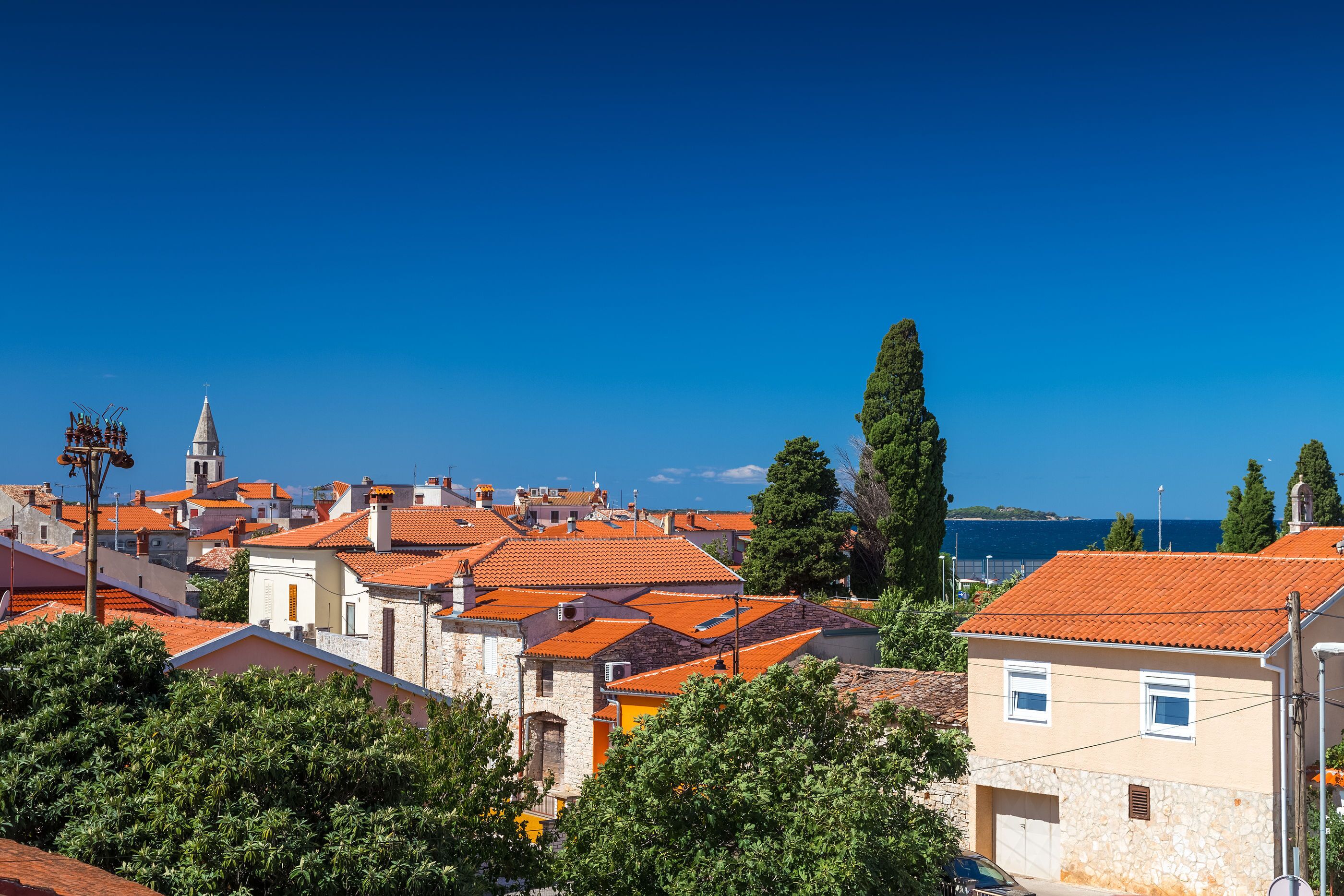Eine Küstenstadt mit traditionellen roten Ziegeldächern, Steinbauten und wolkenlosem, blauem Himmel.