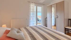 Une chambre à coucher comprenant un lit, une chaise, une armoire et donnant sur l’extérieur.