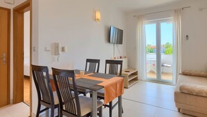 Un salon moderne comprenant un coin repas, un téléviseur à écran plat fixé au mur et une porte-fenêtre coulissante donnant sur un balcon extérieur.