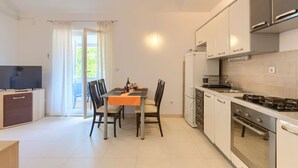 Une cuisine moderne avec un coin repas, comprenant un téléviseur, une table à manger avec des chaises, un réfrigérateur, une cuisinière et des placards.