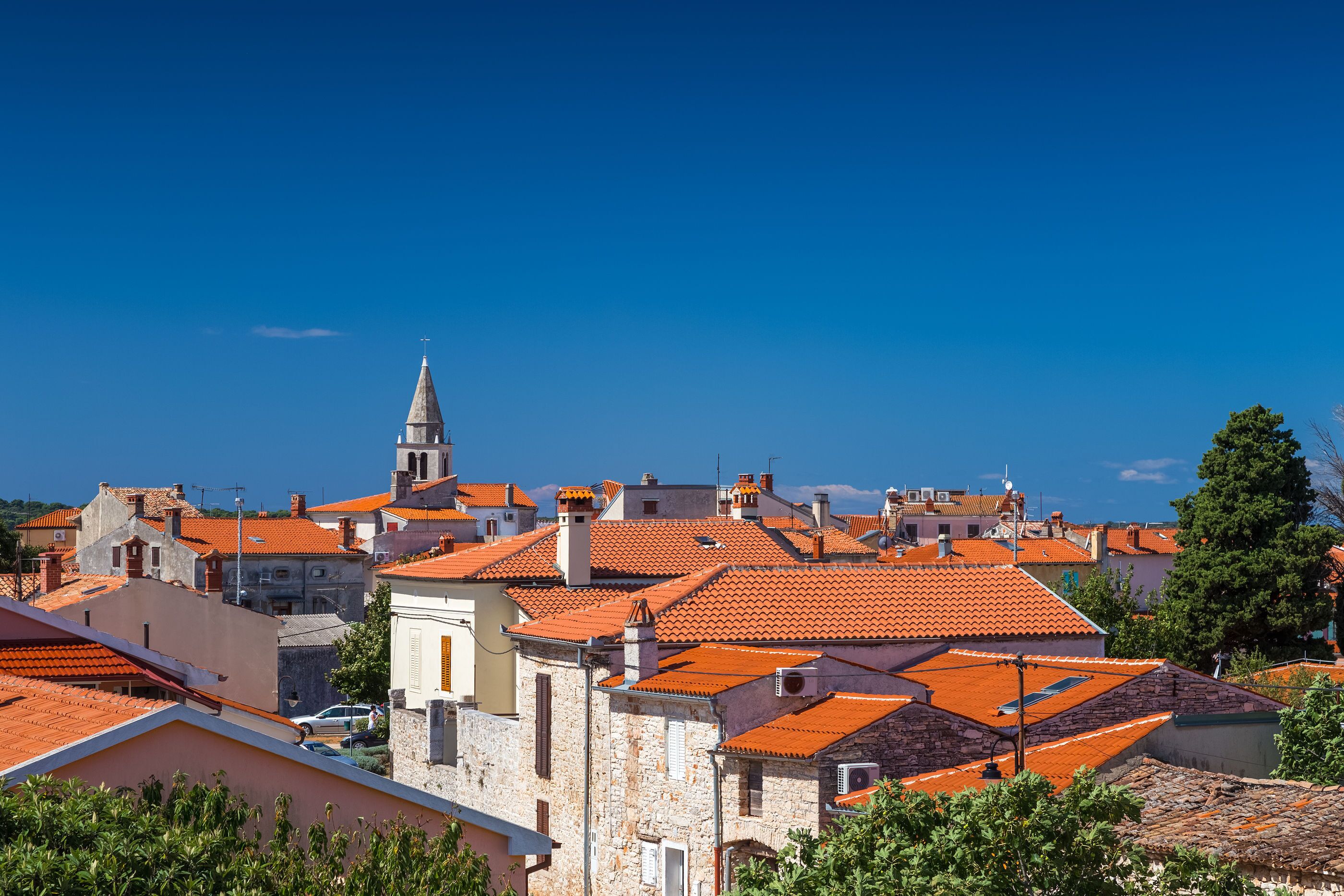 A town with red-tiled roofs and stone buildings, featuring a prominent church steeple.
