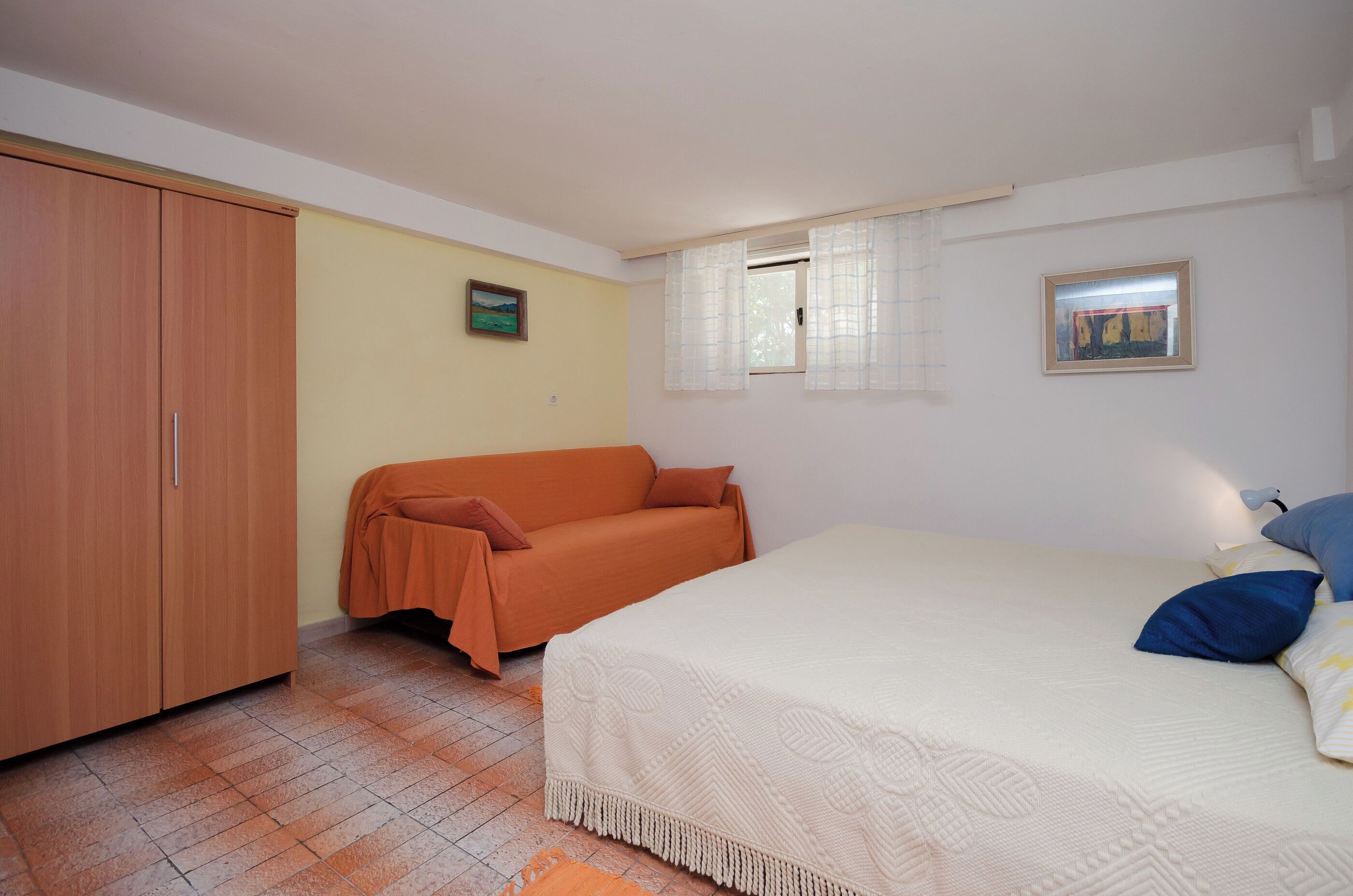 A bedroom with a bed, a sofa, a wardrobe, and two windows.
