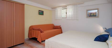 A bedroom with a bed, a sofa, a wardrobe, and two windows.