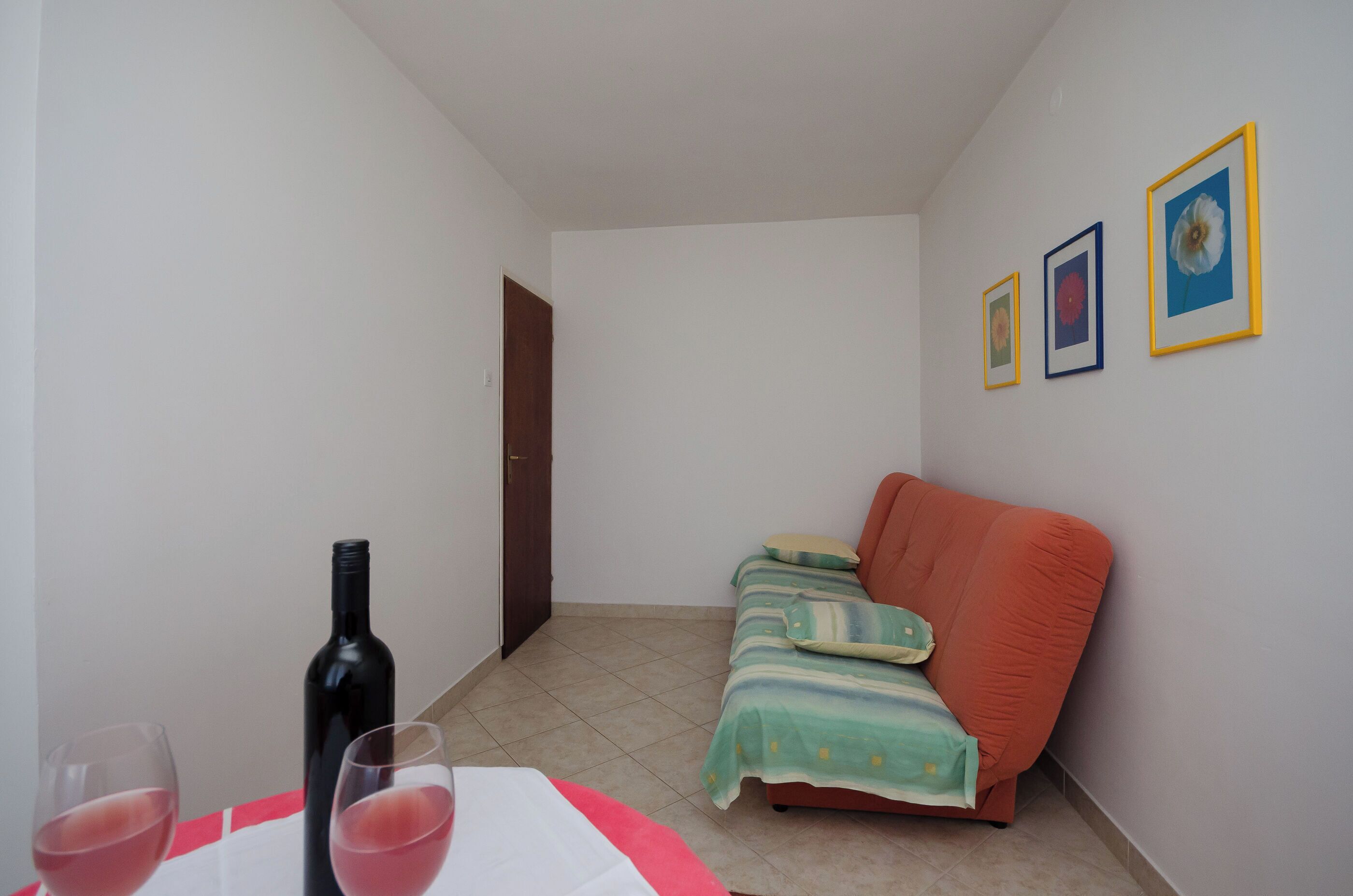 Een kleine kamer met een bed, een tafel met een wijnfles en glazen, en drie ingelijste foto’s aan de muur.