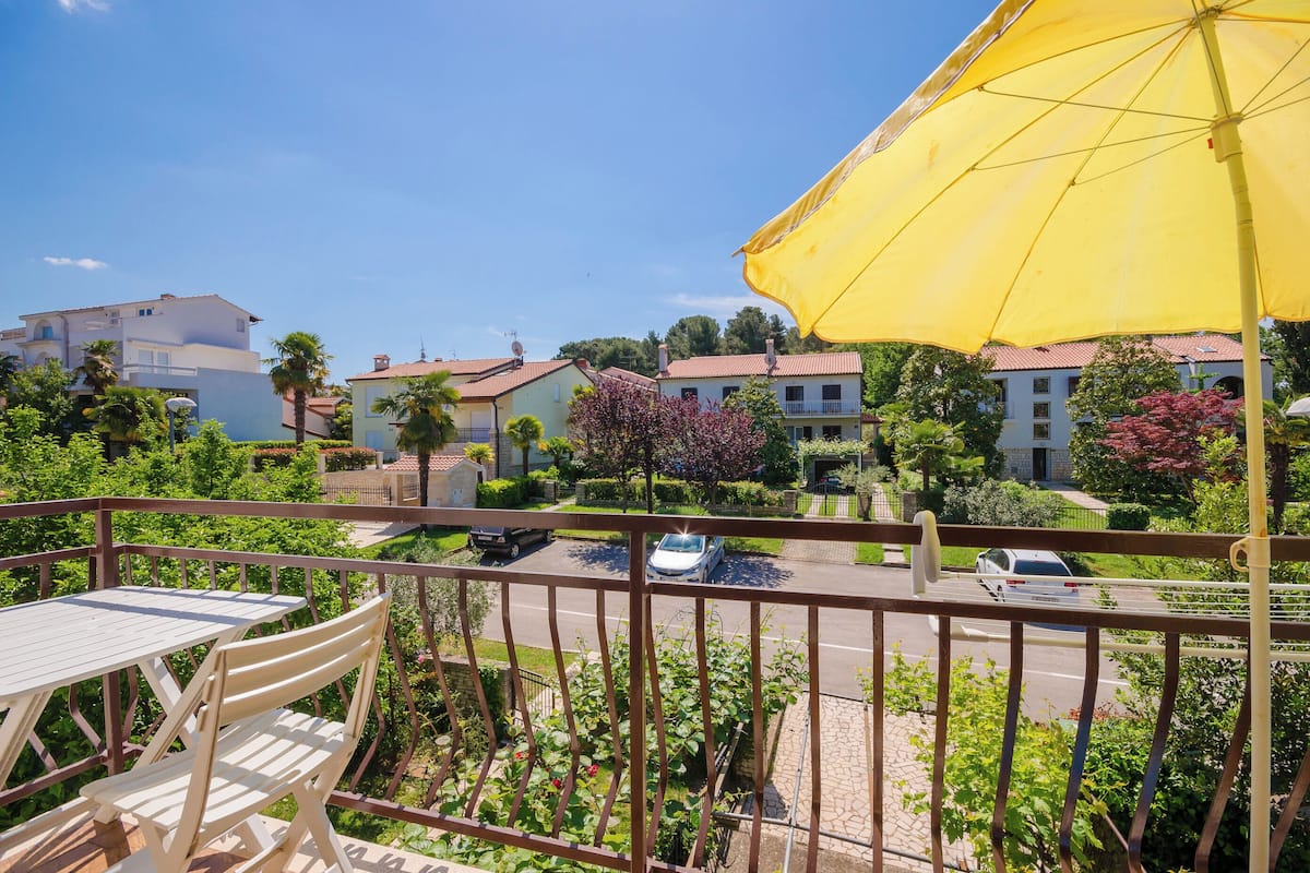 Un balcon avec un parasol jaune, une table et des chaises.