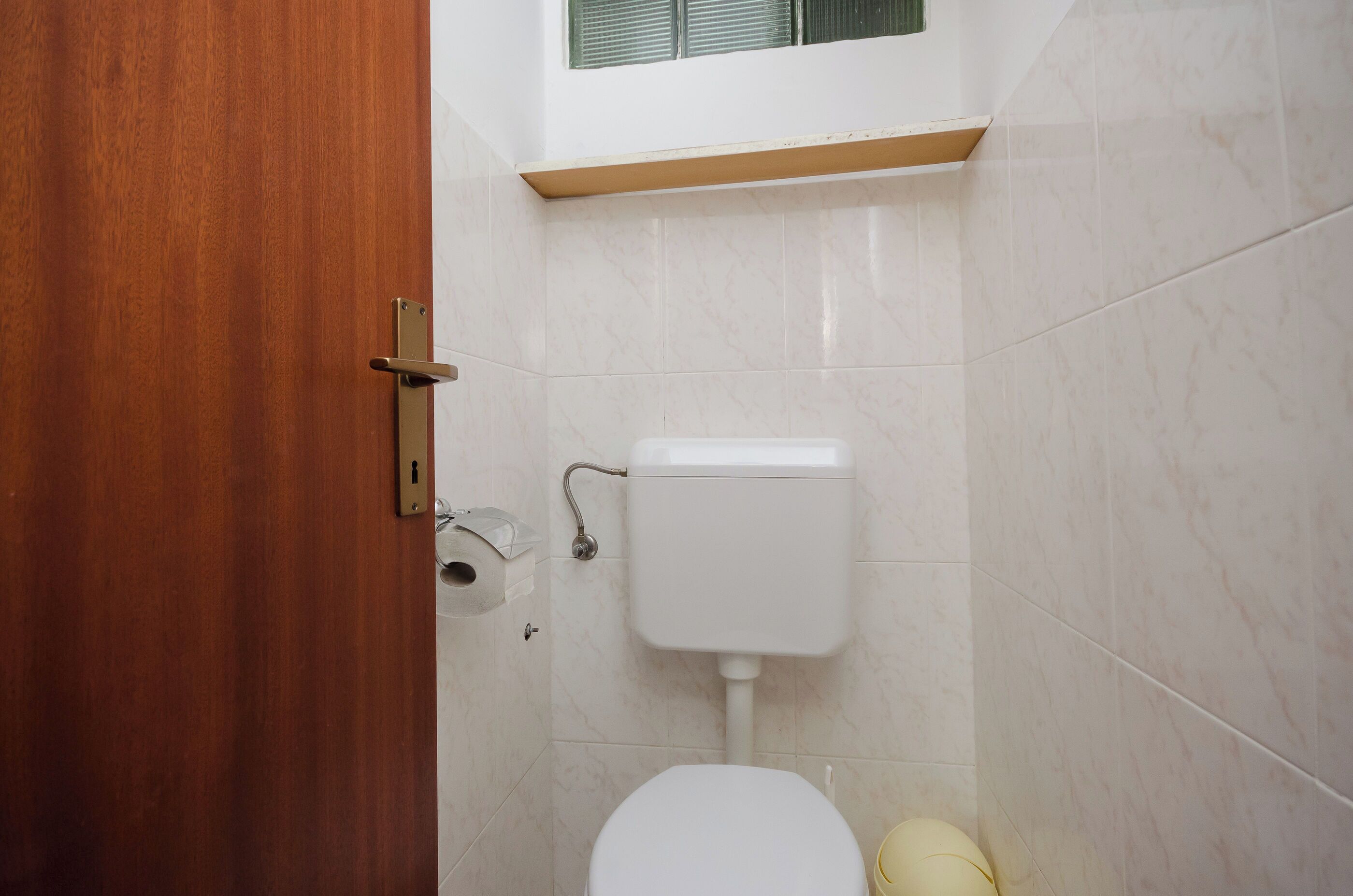A bathroom with a toilet, a wooden door, and a window above the toilet.
