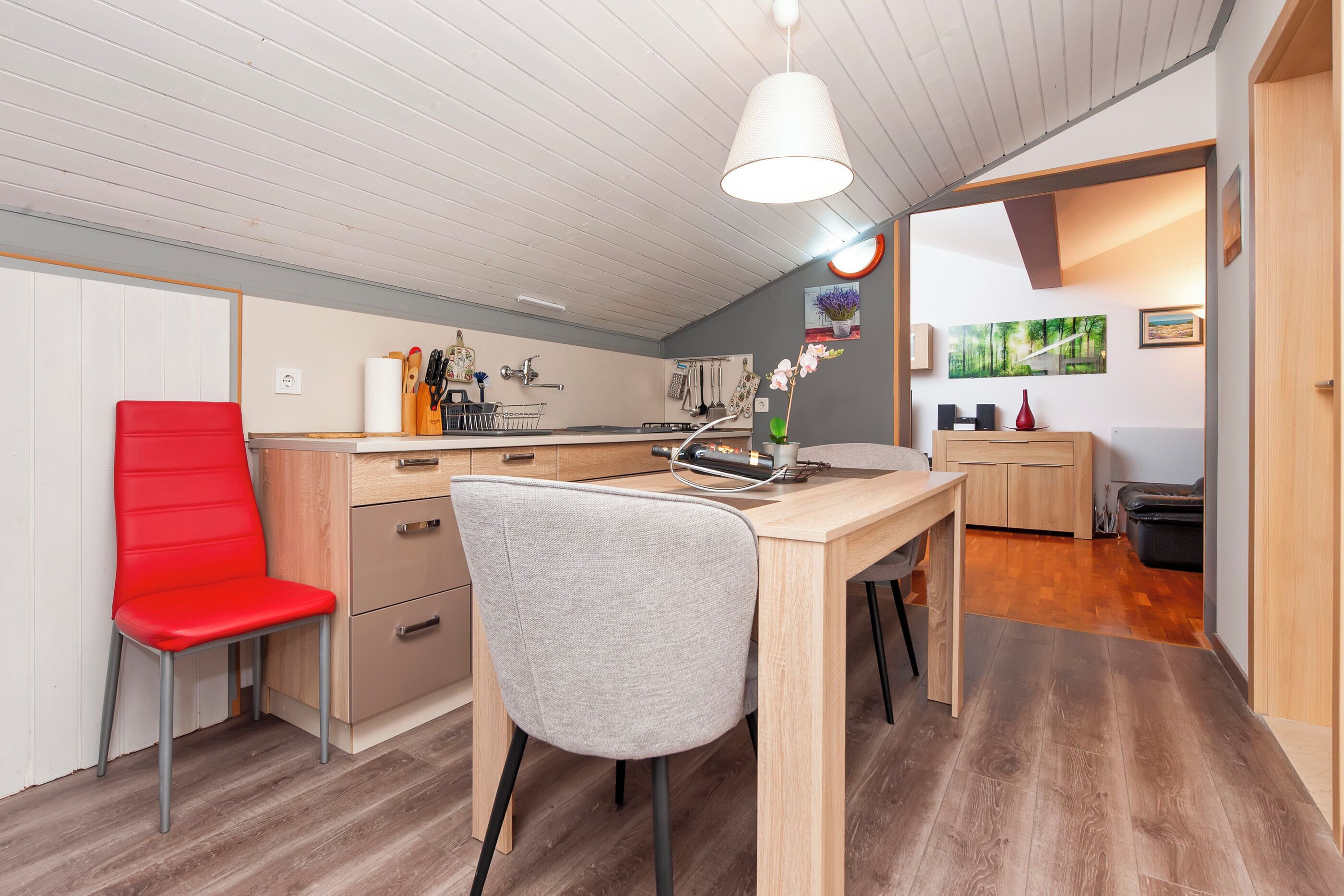 Une cuisine moderne avec des meubles de rangement en bois, une chaise rouge et une chaise grise.