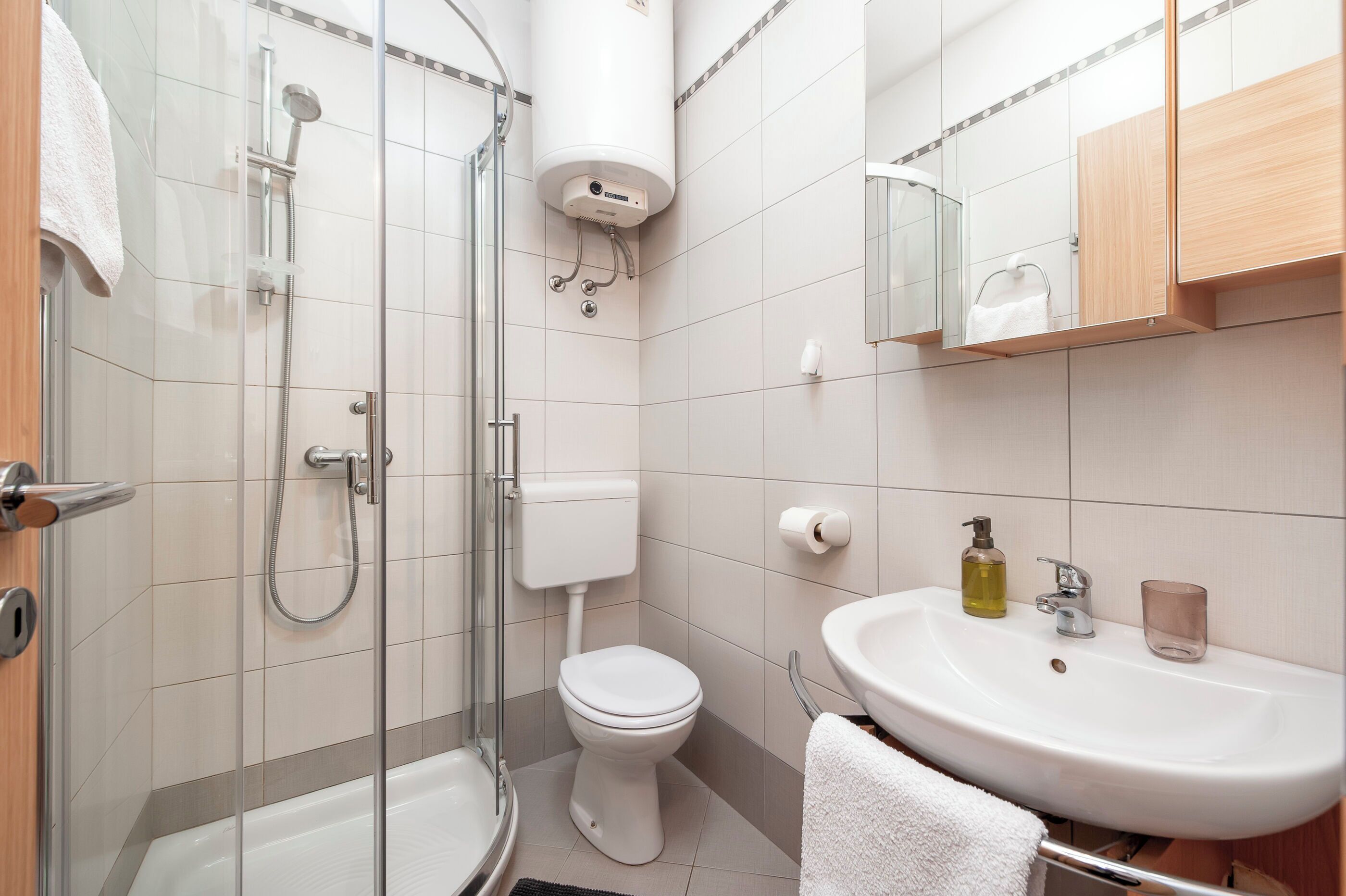 A modern bathroom with a glass-enclosed shower, a toilet, and a sink with a mirror above.