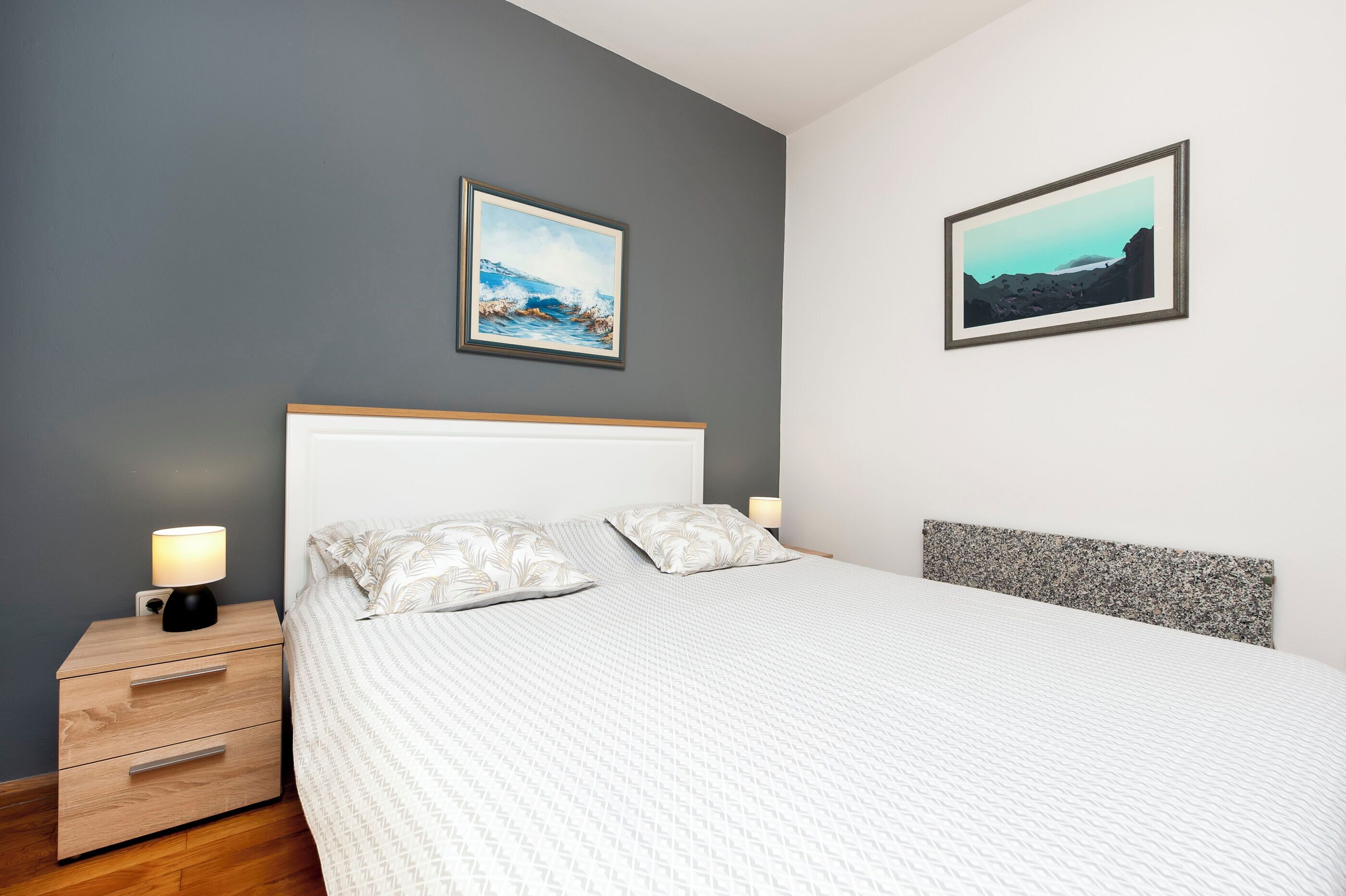 Une chambre à coucher avec un lit, des tables de chevet et deux tableaux accrochés au mur.