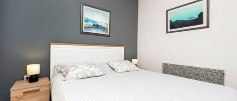 Une chambre à coucher avec un lit, des tables de chevet et deux tableaux accrochés au mur.