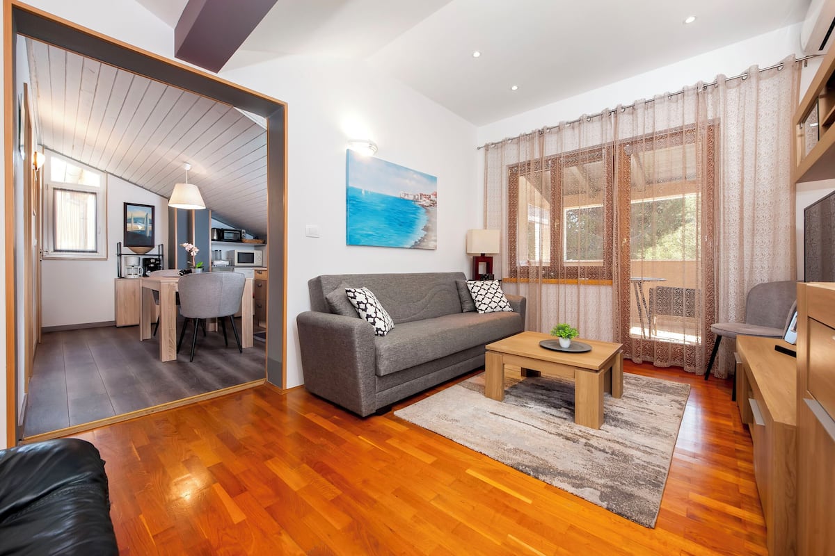 A modern living room with a grey sofa, wooden coffee table, and a view of the kitchen and dining area.