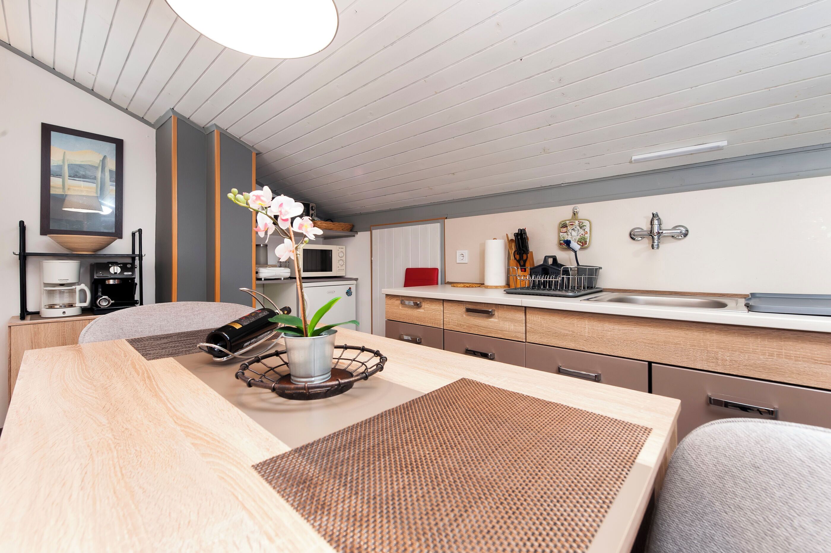 A modern kitchen with a wooden table, a coffee machine, a microwave, and a sink.