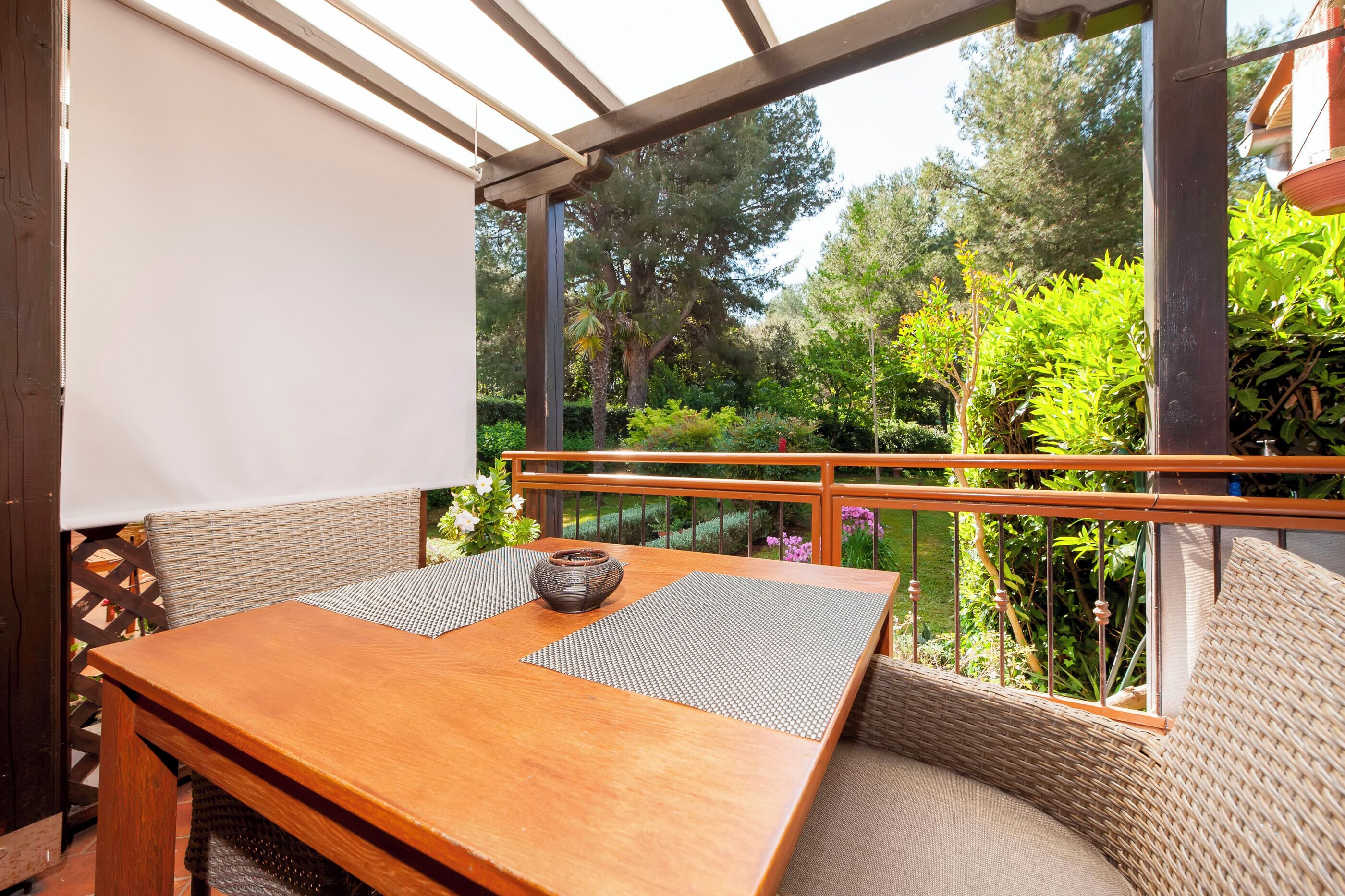 A wooden table with a woven cushion and a bowl, set against a backdrop of lush greenery and a wooden railing.