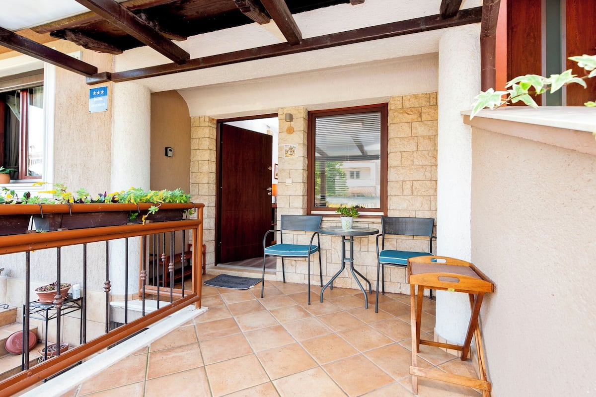 A patio with a wooden table and chairs, a small wooden stool, and potted plants.