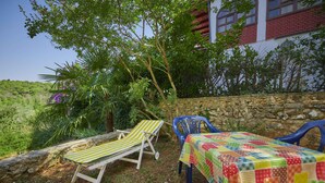 A patio with a table and chairs, surrounded by greenery and a stone wall. - Apartments Davorka (Banjole)