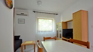 Ein Zimmer mit Esstisch, Stühlen, Fernseher, einer Couch und einem Fenster mit Vorhängen.