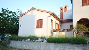 Ein zweistöckiges Gebäude mit weißer Fassade, braunen Fensterläden und einem kleinen Balkon mit Metallgeländer.