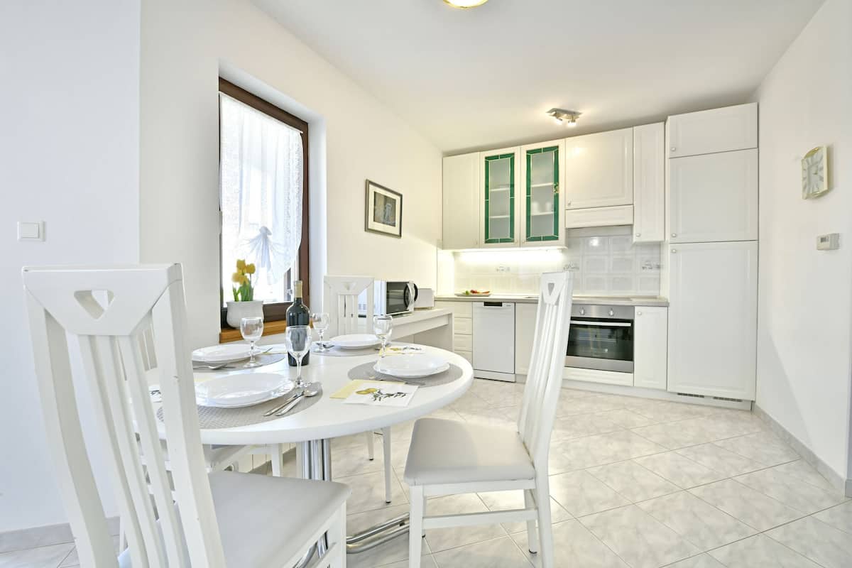 A modern kitchen with white cabinets, a dining table set for four, and a window with curtains.