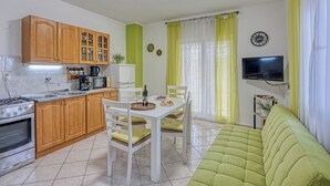 Eine kompakte Küche mit Holzausstattung, einem Esstisch mit Stühlen, einem grünen Sofa, einem Fernseher und einem kleinen Regal mit einer Pflanze.