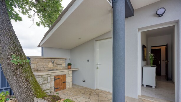 Ein modernes Haus mit Kamin aus Stein, einer Tür und einem kleinen Gartenbereich mit Blumentöpfen.