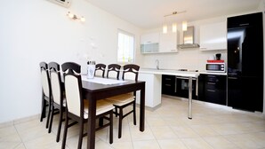 A modern kitchen with white cabinets, a black refrigerator, and a dining area with a wooden table and chairs. - Apartment Bungalov (Rovinj)