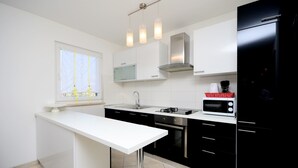 A modern kitchen with a white countertop, black cabinets, stainless steel appliances, and pendant lighting. - Apartment Bungalov (Rovinj)