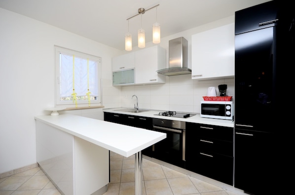 A modern kitchen with a white countertop, black cabinets, stainless steel appliances, and pendant lighting. - Apartment Bungalov (Rovinj)