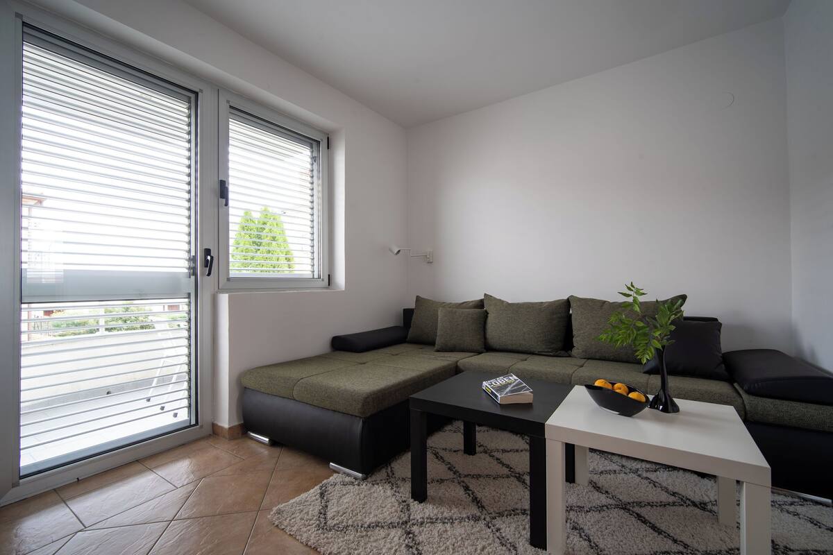 A modern living room with a sectional sofa, a coffee table, and a window with blinds.