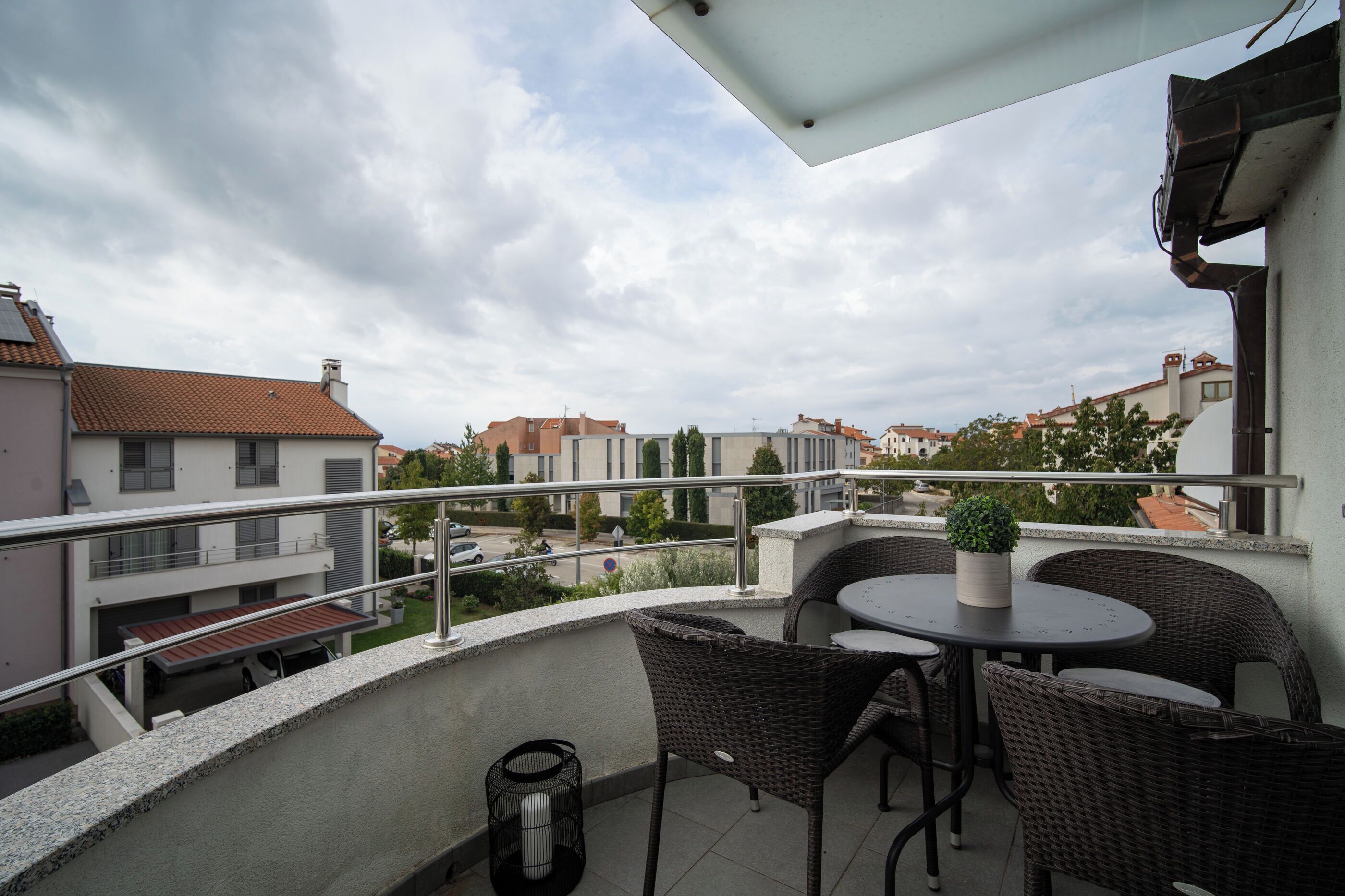 A balcony with wicker furniture, a potted plant, and a view of neighboring buildings.