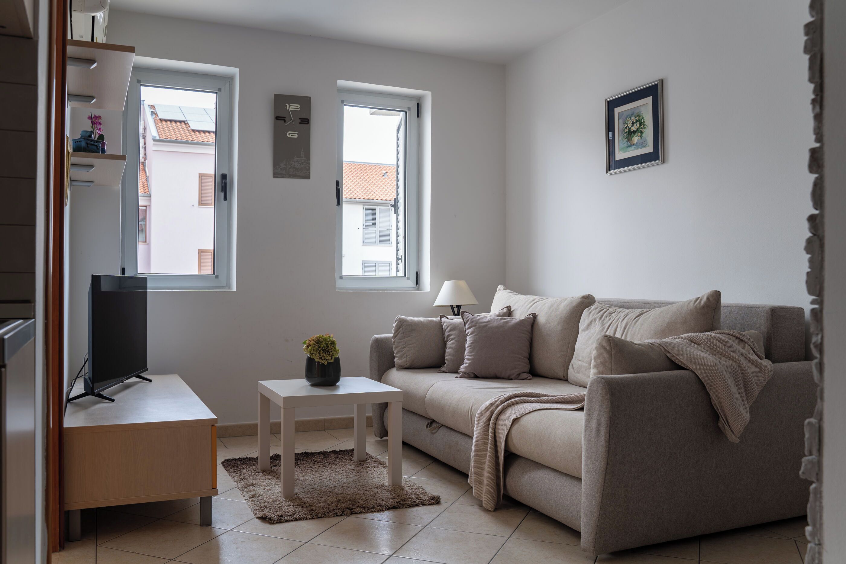 A modern living room with a sofa, a small table, a TV, and two windows.
