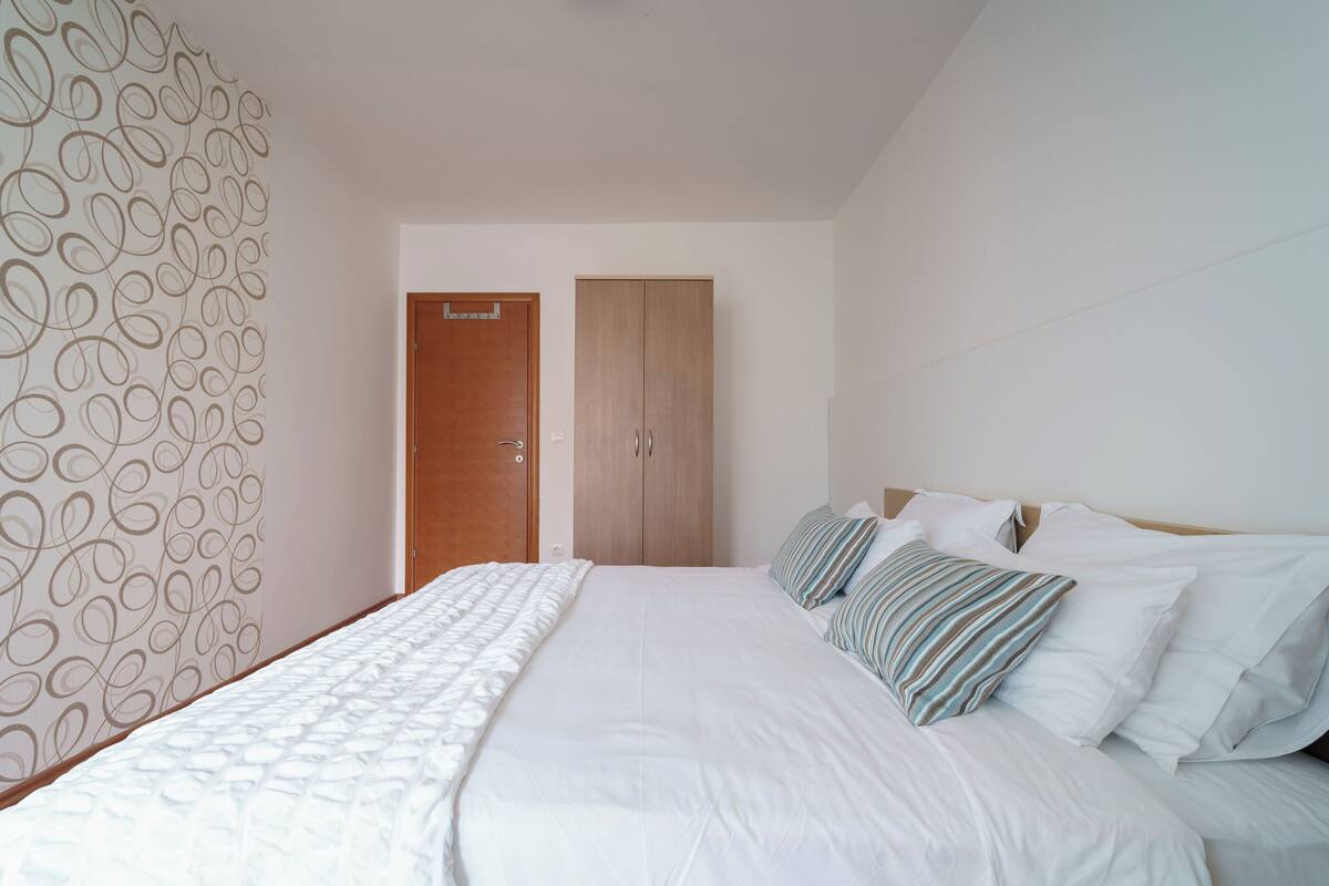 A bedroom with a bed, pillows, a wardrobe, and a door.