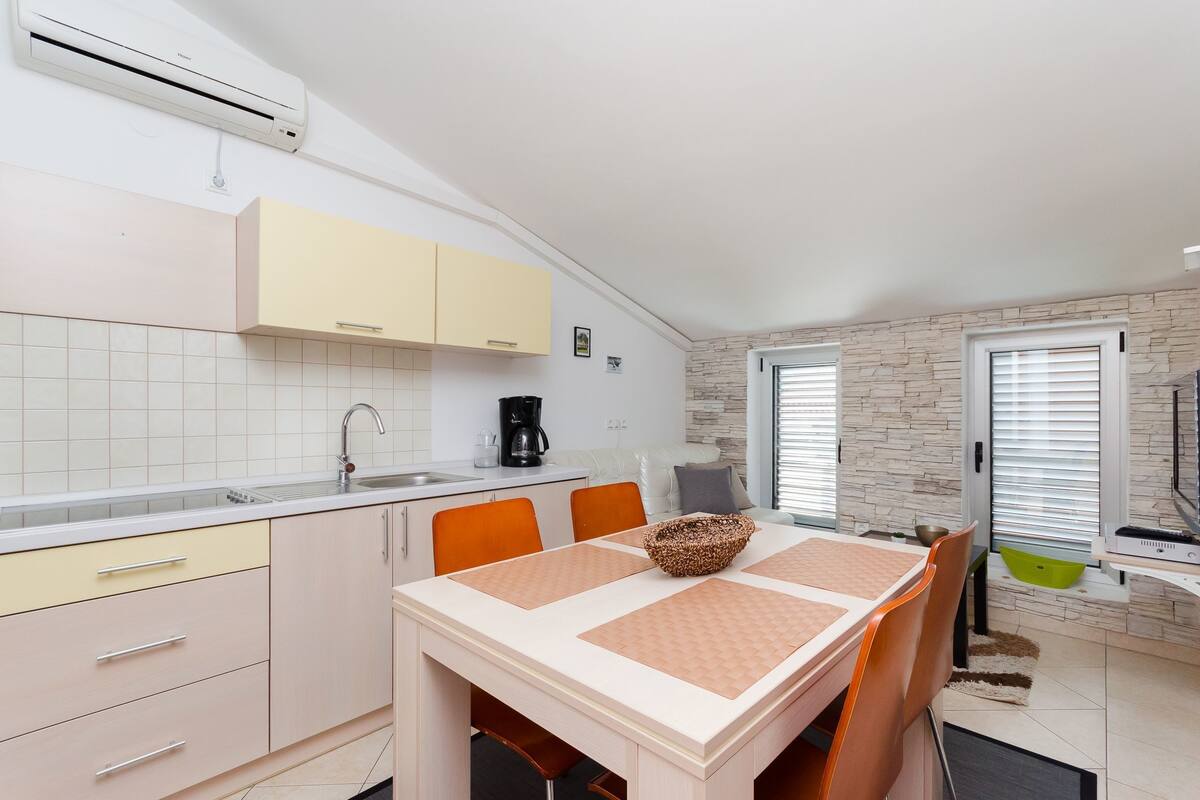 A modern kitchen with a dining area, featuring a white tiled backsplash, beige cabinets, and a stone accent wall.