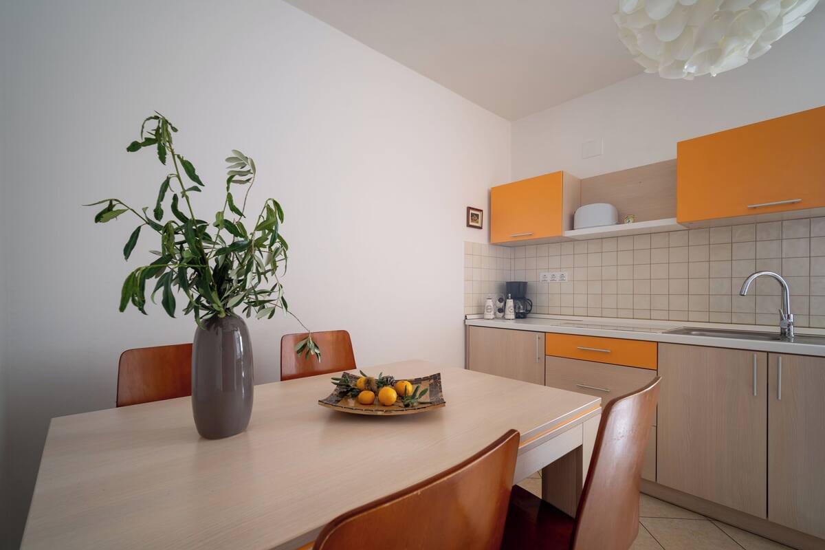 A modern kitchen with wooden cabinets, a white countertop, and a dining area with a table and chairs.