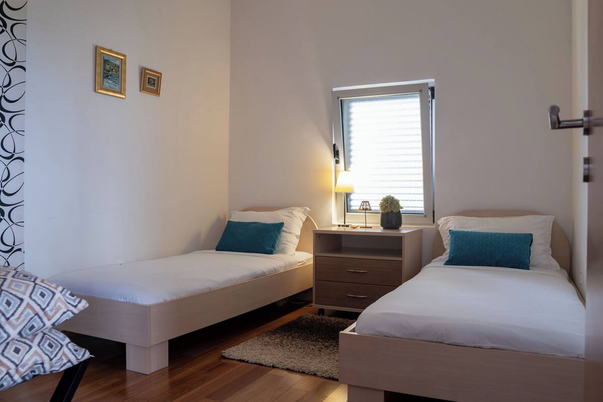 A twin bedroom with two beds, a nightstand, a window, and a door.
