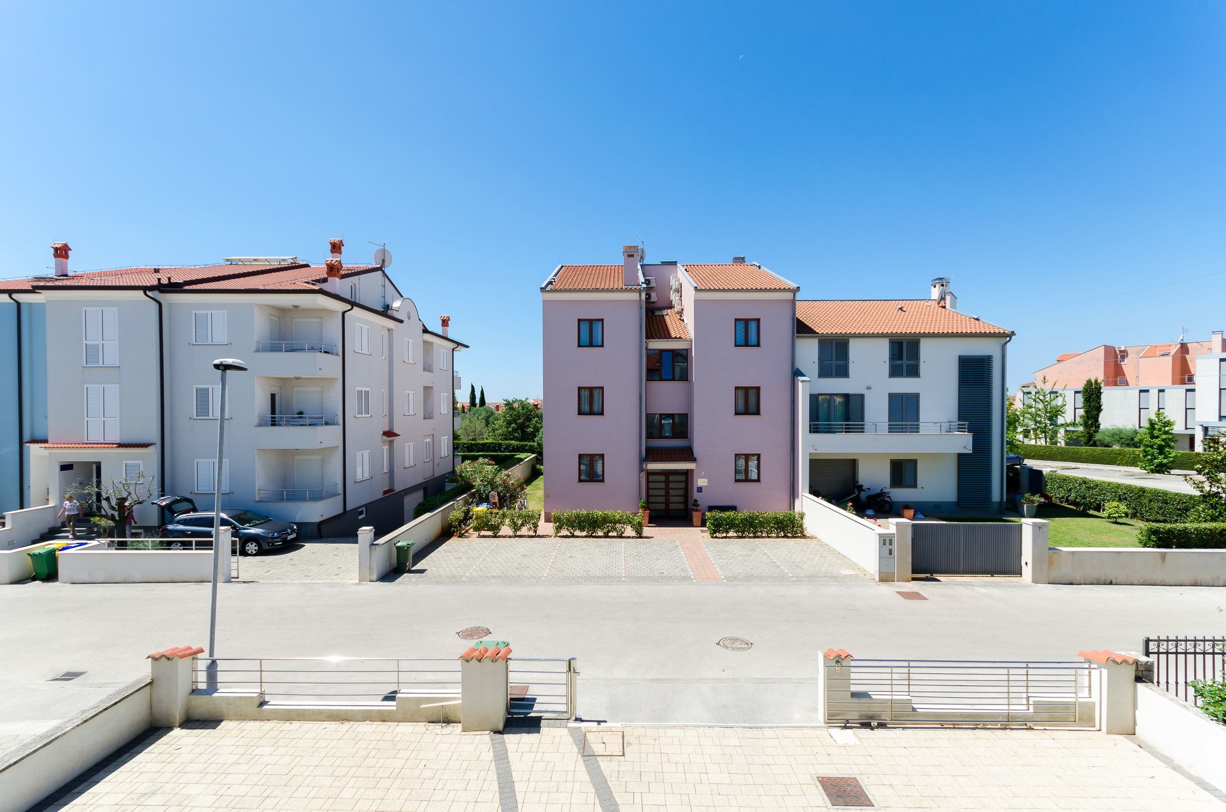 A residential building with a central entrance, a paved driveway, and a gated parking area.