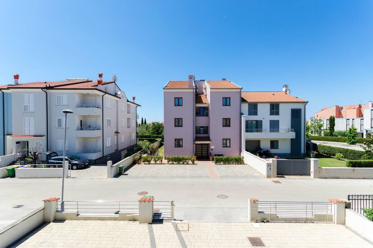 A residential building with a central entrance, a paved driveway, and a gated parking area.