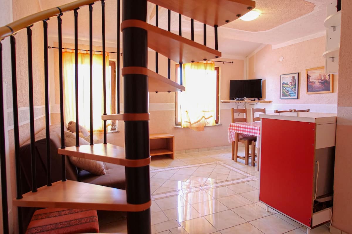 Un salon avec un escalier en bois, un téléviseur, une table à manger avec des chaises et un buffet rouge.