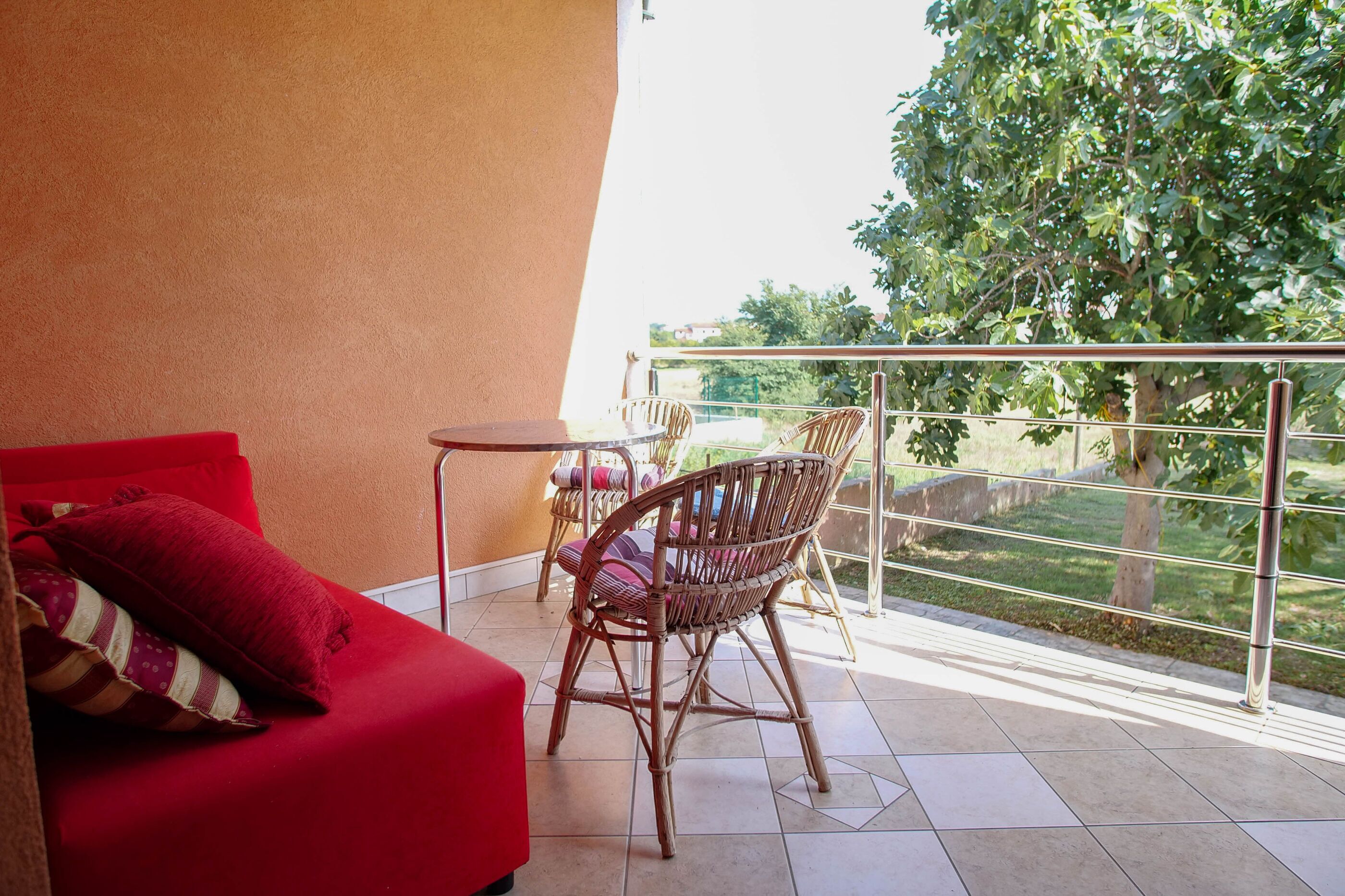 Un balcon avec un canapé rouge, des fauteuils en osier et une petite table.