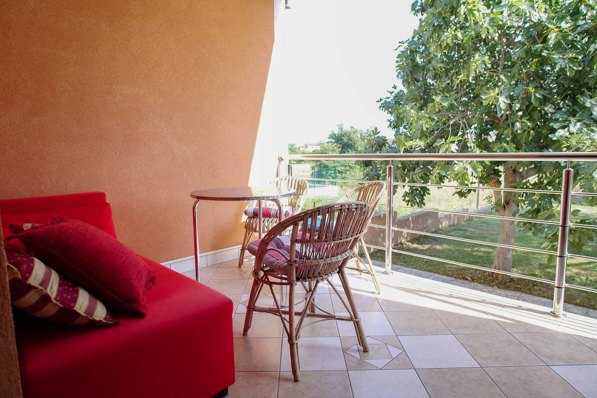 Un balcon avec un canapé rouge, des fauteuils en osier et une petite table.