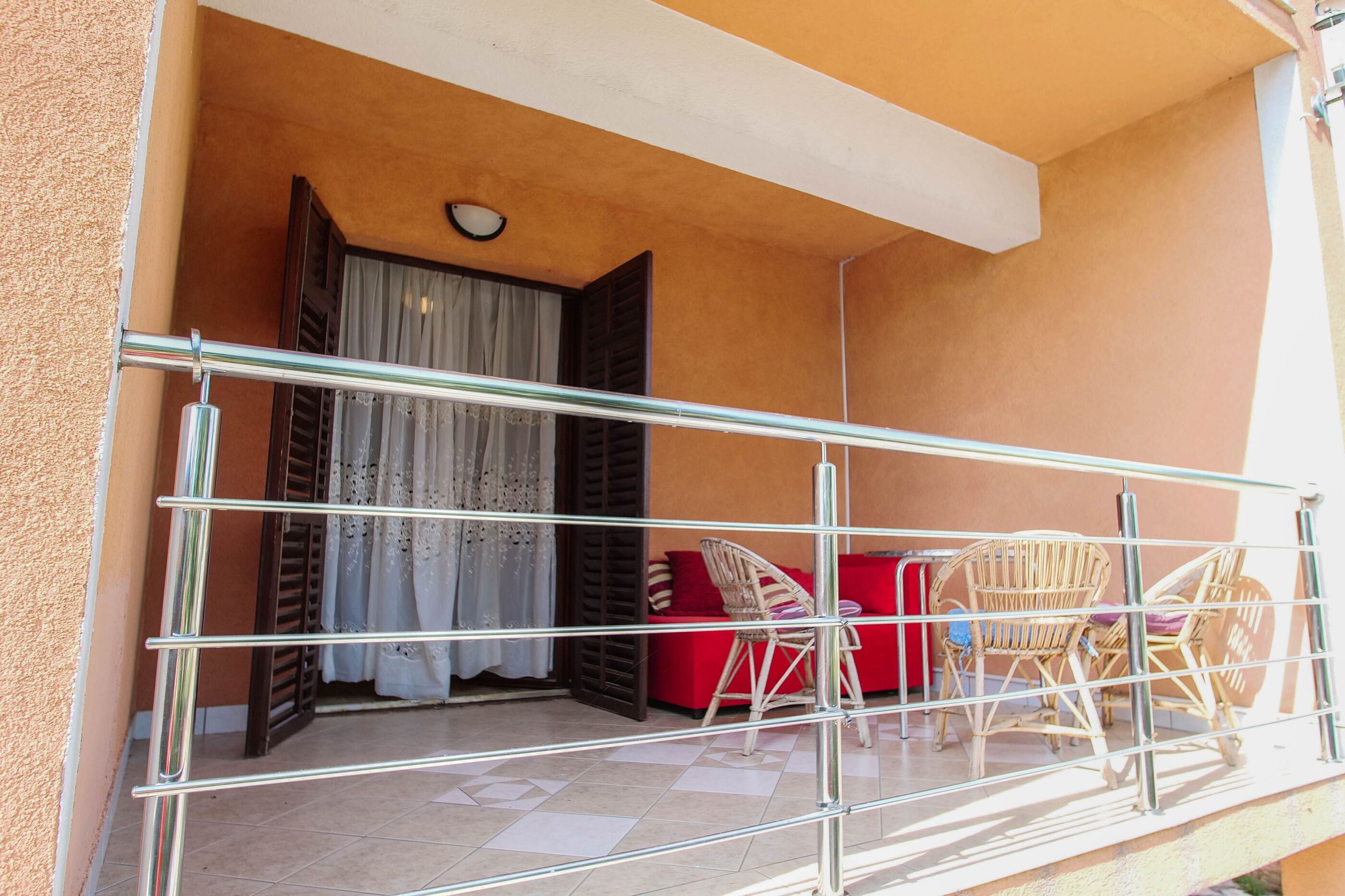 A balcony with a metal railing, a red sofa, wicker chairs, and a window with curtains.