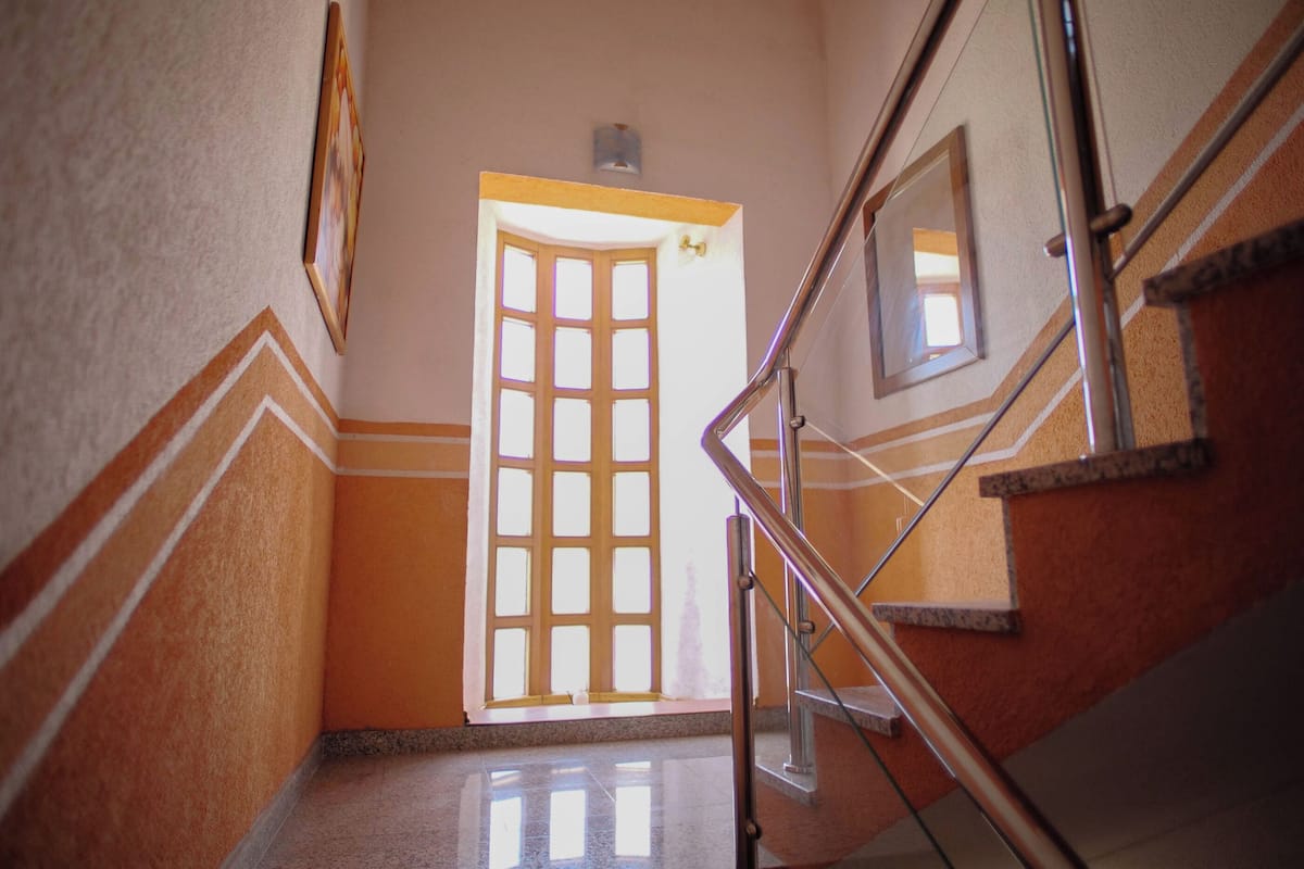 Un escalier avec une rampe, une porte avec une fenêtre et un mur orné d’un motif géométrique.