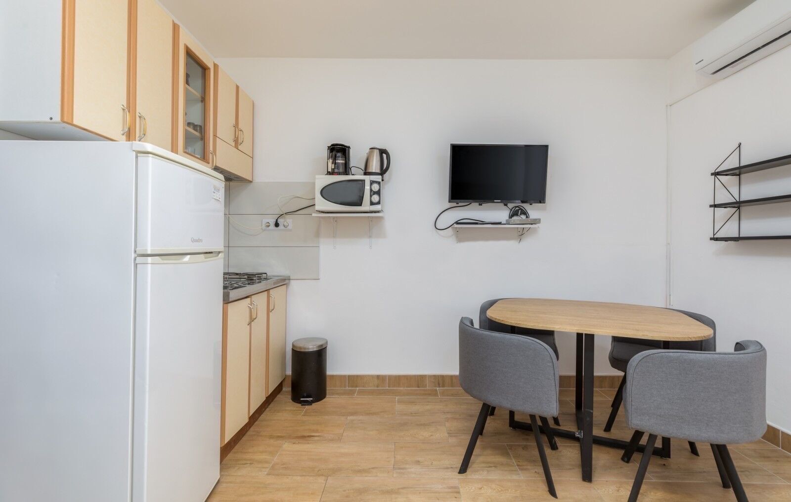A compact kitchen with a refrigerator, microwave, and stove, a small trash bin, and a dining table with two chairs.