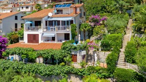 A multi-story building with balconies, surrounded by lush greenery and a staircase leading up. - Apartments Mandica (Rabac)