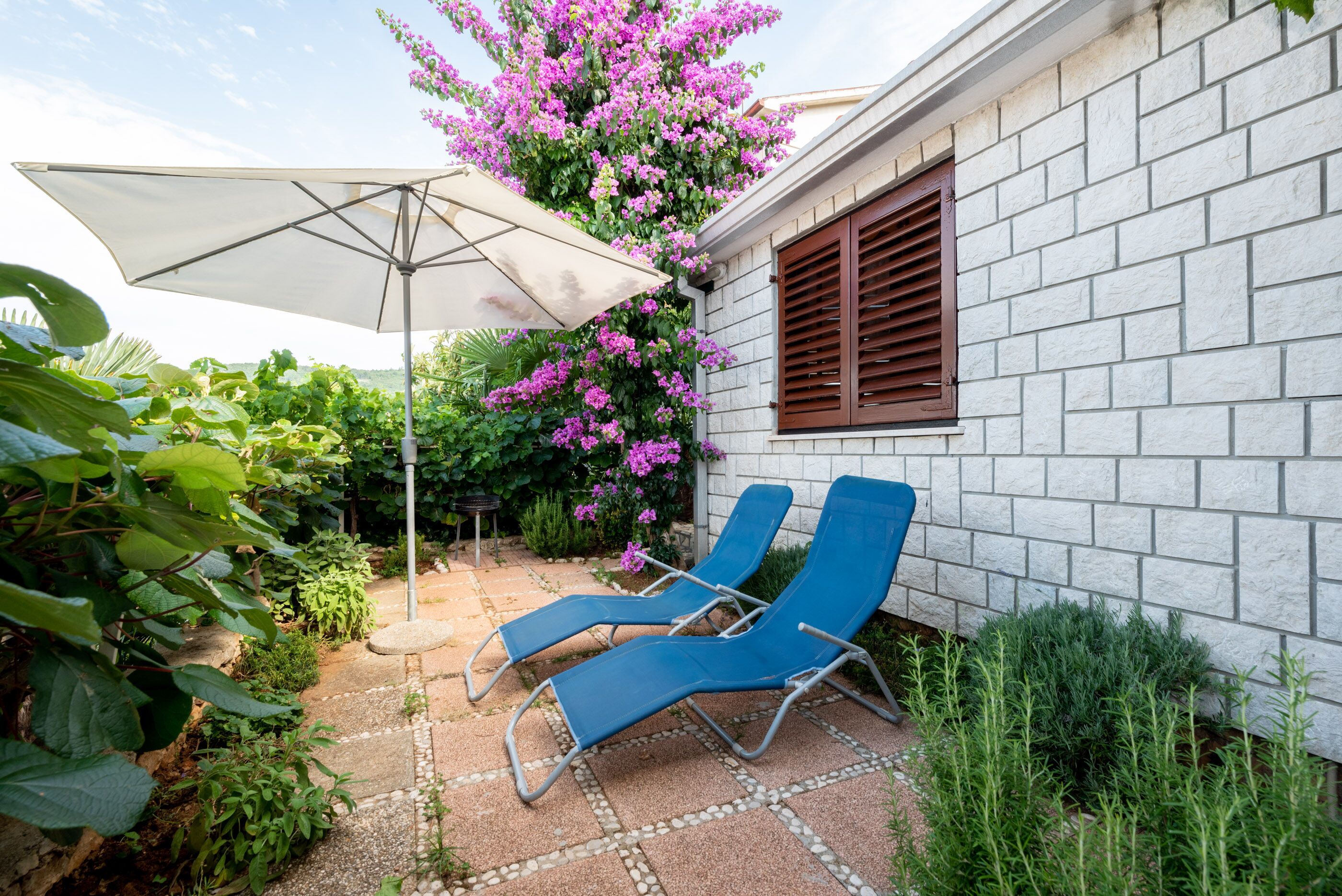 A patio with two blue lounge chairs, a white umbrella, and a white brick wall.