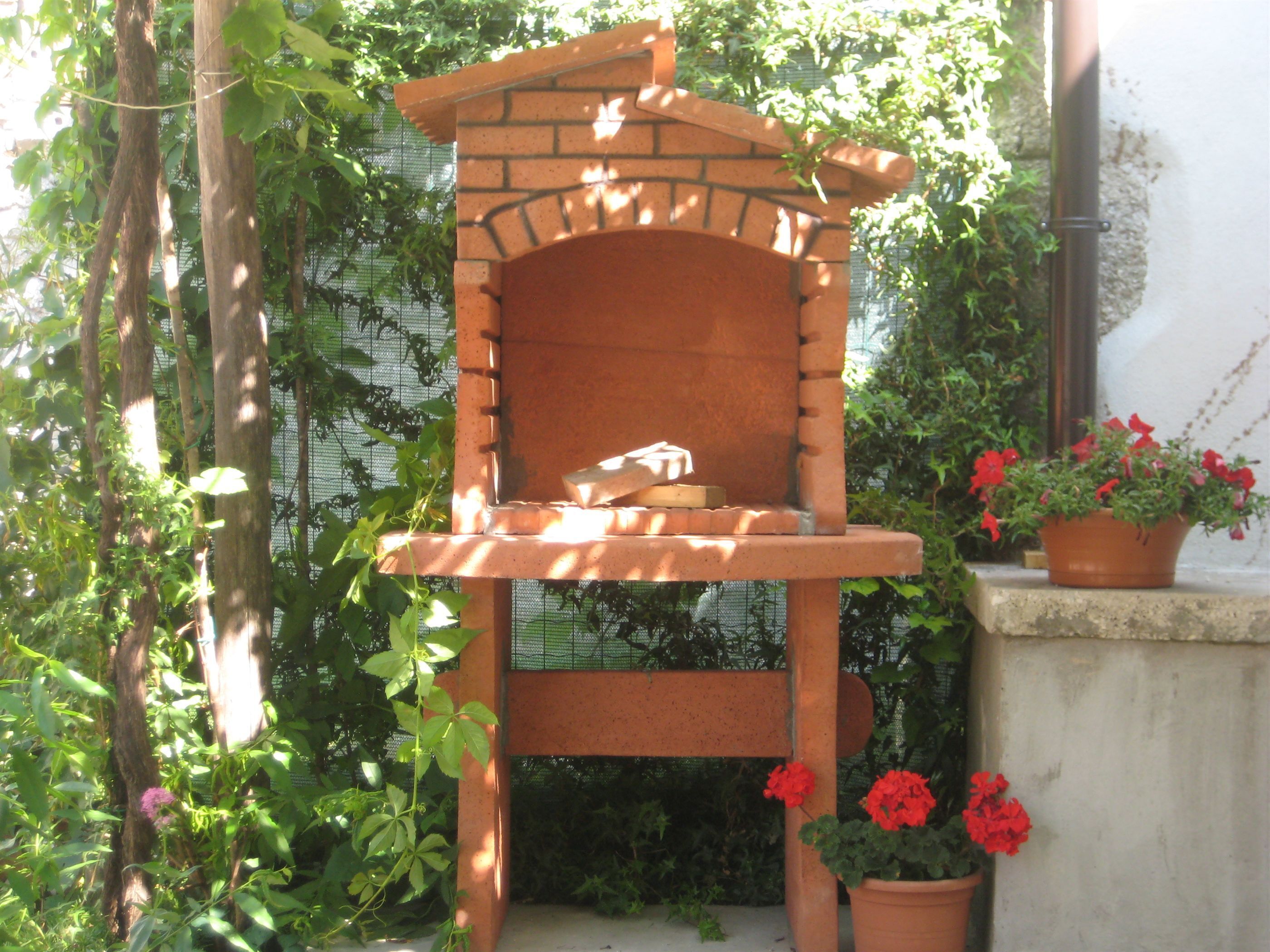 A brick-built outdoor seating area with a bench, surrounded by greenery and potted plants.