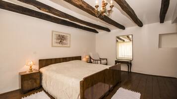 Un dormitorio con una cama de madera, una mesita de noche con lámpara, una silla, un espejo y una araña.